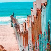 A border wall painted different colors blocking a section of beach with the ocean visible. 