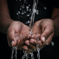 Dark-skinned person cupping hands under a stream of water. 
