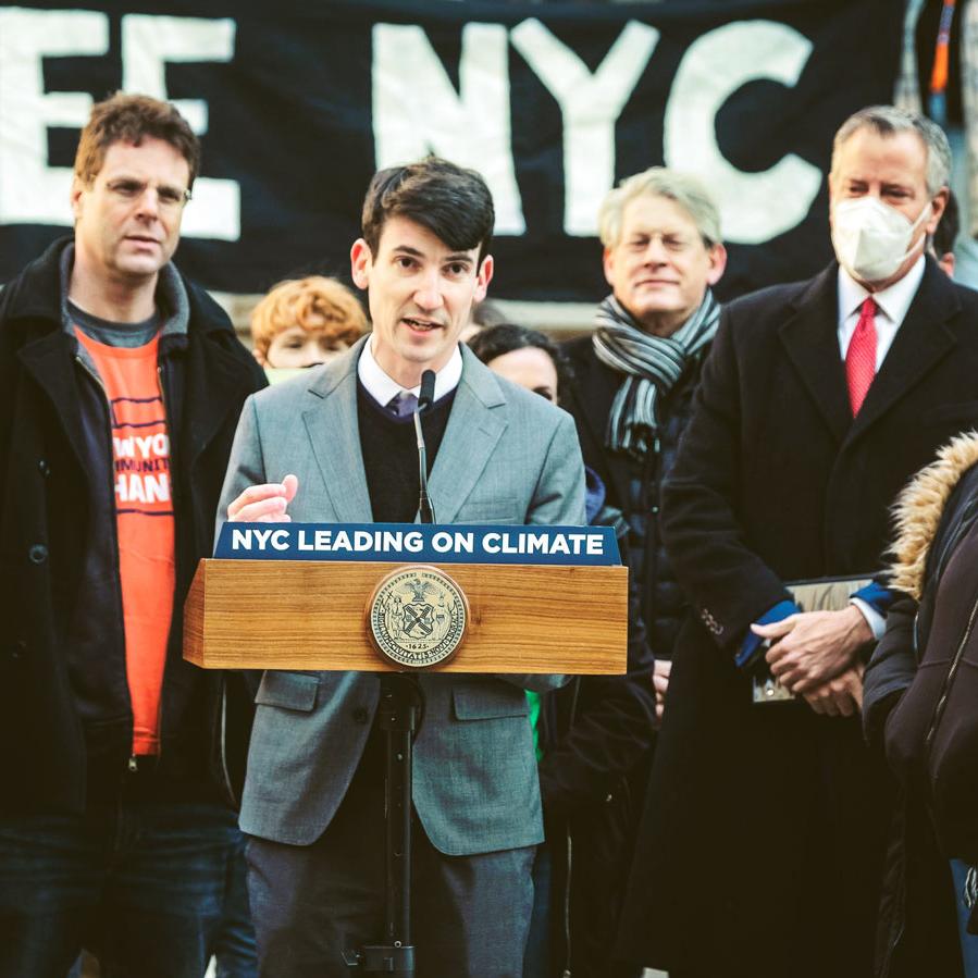 Person wearing gray suit speaks at a podium that says 'NYC LEADING ON CLIMATE'