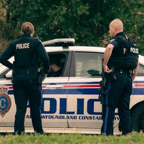 Two police officers stand near a police car