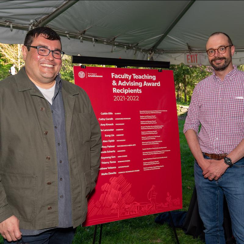 Two people stand near a poster listing awards