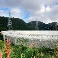 Giant white dish-shaped structure set in lush hills
