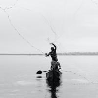 Person casts a net from a canoe on a calm lake