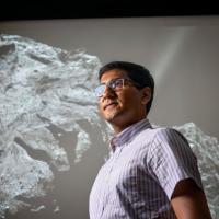Person standing in front of a huge black & white image of a comet with a rocky surface