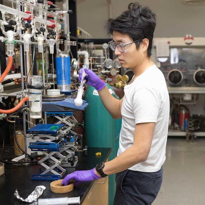 Person working in a lab, wearing safety goggles and purple gloves