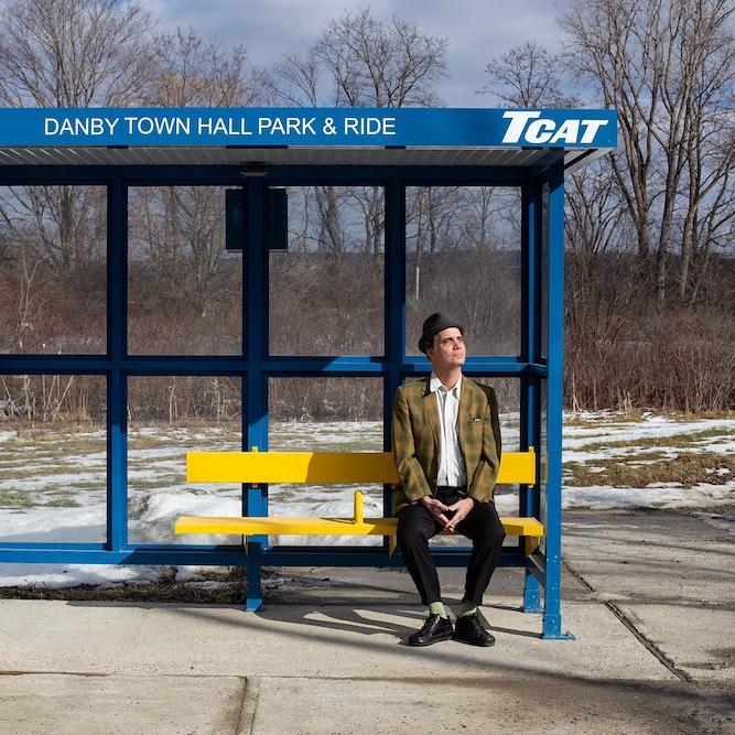 Person in plaid jacket sits at a bus stop
