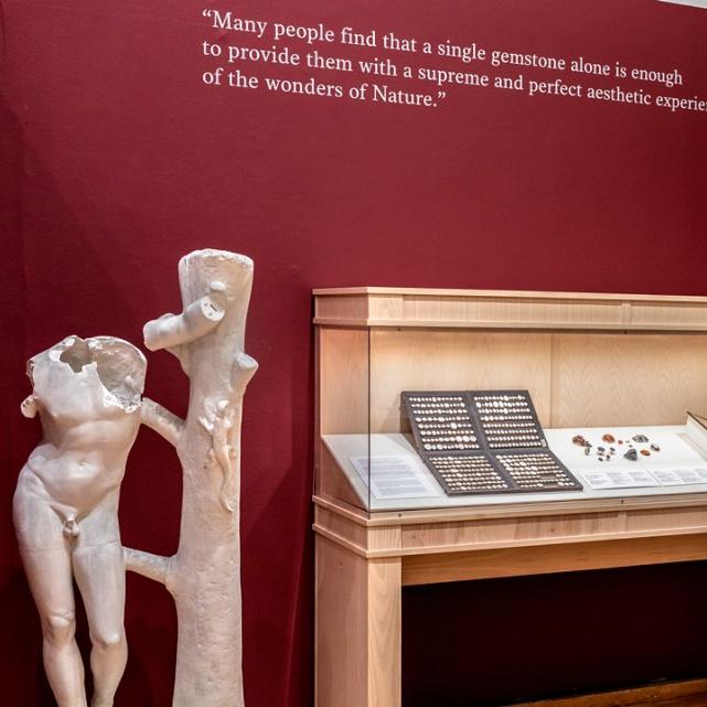 Museum display of a nude sculpture, cases of objects and a quote on the wall
