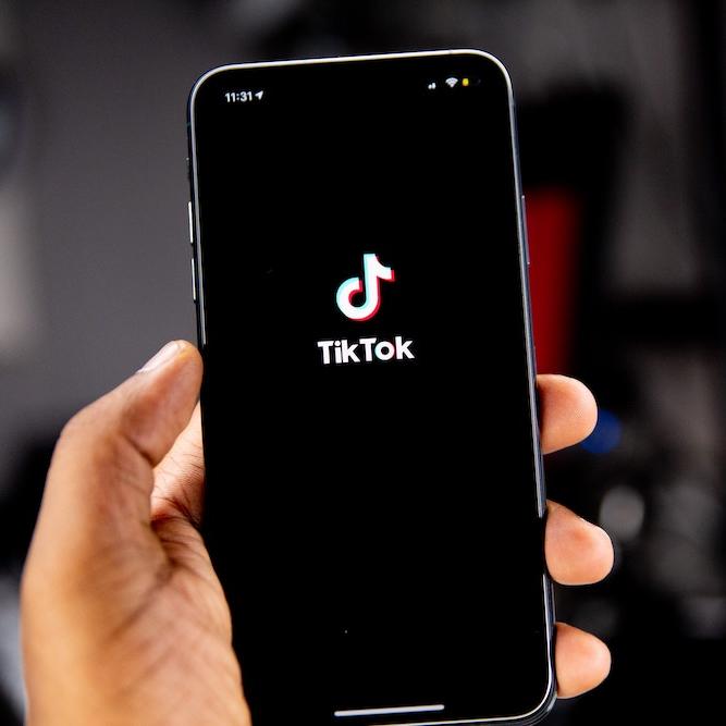 		Hand holding a smart phone showing the TikTok icon
	