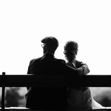 Black and white image of two people sitting on a bench, seen from behind