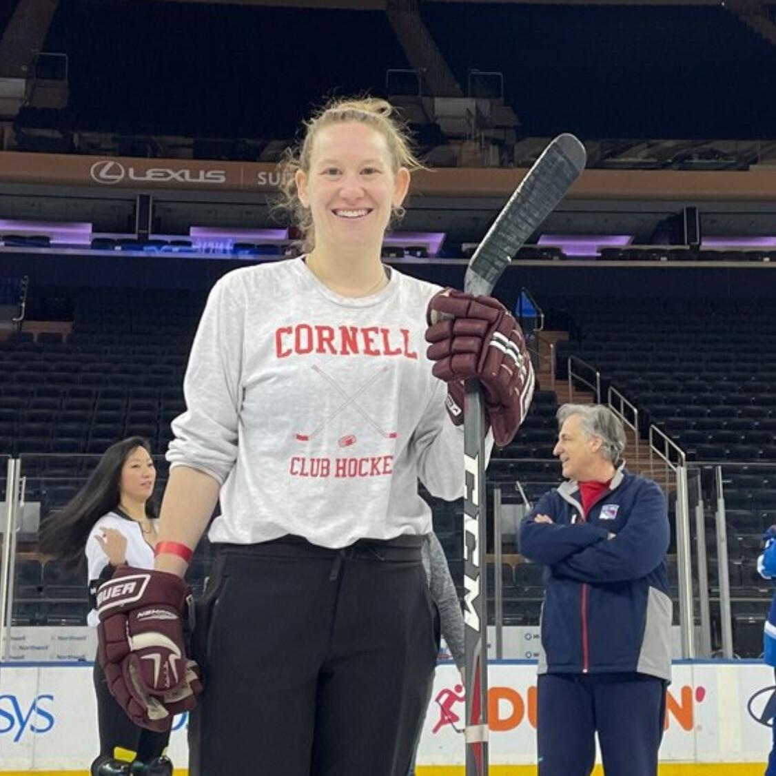 		Person wearing hockey gloves and a Cornell t-shirt, carrying a hockey stick and smiling
	