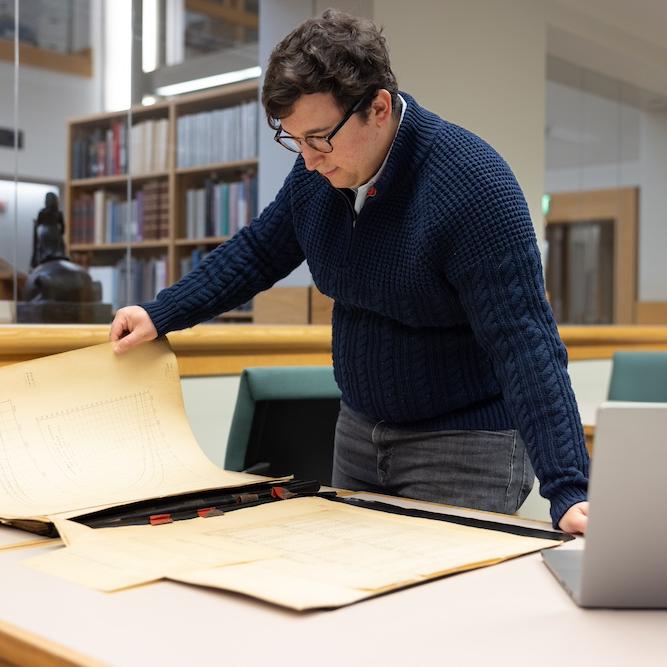 Person holds a large, yellowed document in a library setting