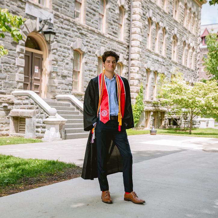 		Smiling photo of smiling man with Cornell graduation gown in front of academic builing.
	