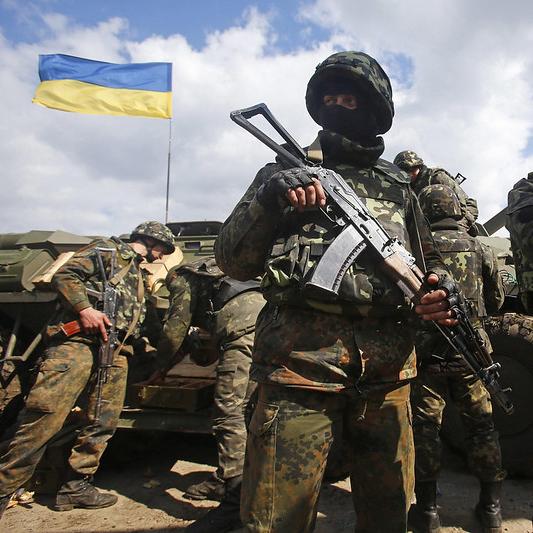 		Several soldiers cluster near a tank; a blue and yellow Ukraine flag flies nearby 
	