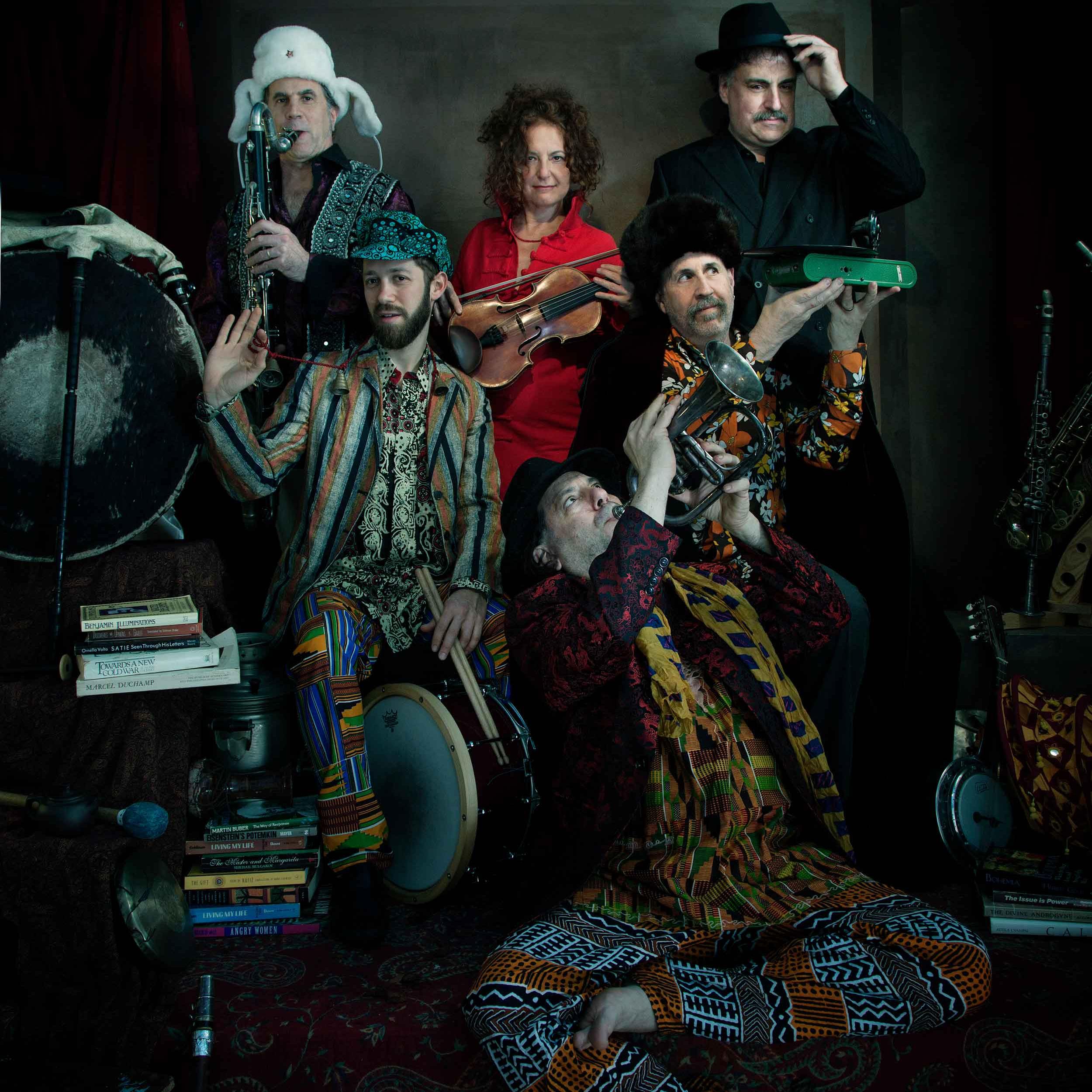 		Six people in colorful, odd clothing, holding and playing musical instruments including fiddle, trumpet and saxophone
	