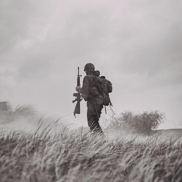 		Soldier in uniform with backpack holding rifle walking across grasslands
	