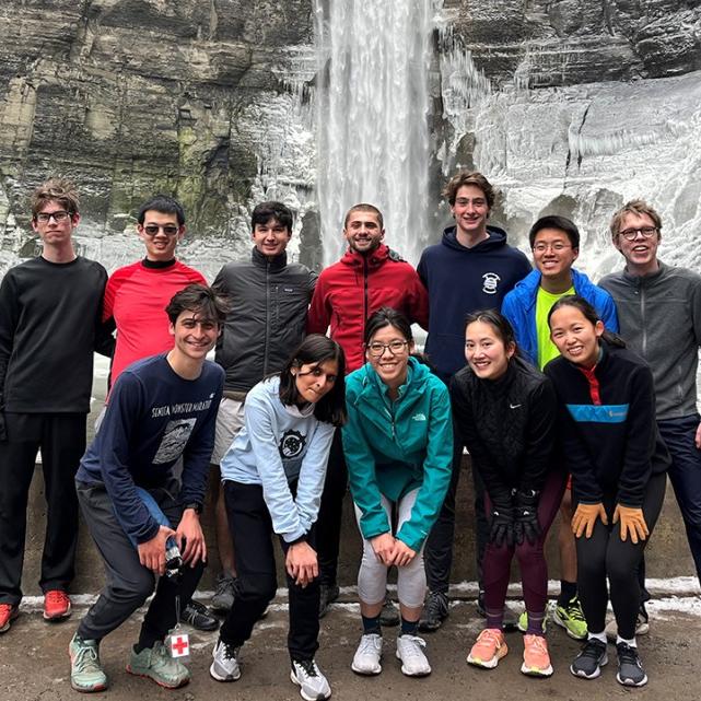 		Several people in running clothes pose at the base of a waterfall
	