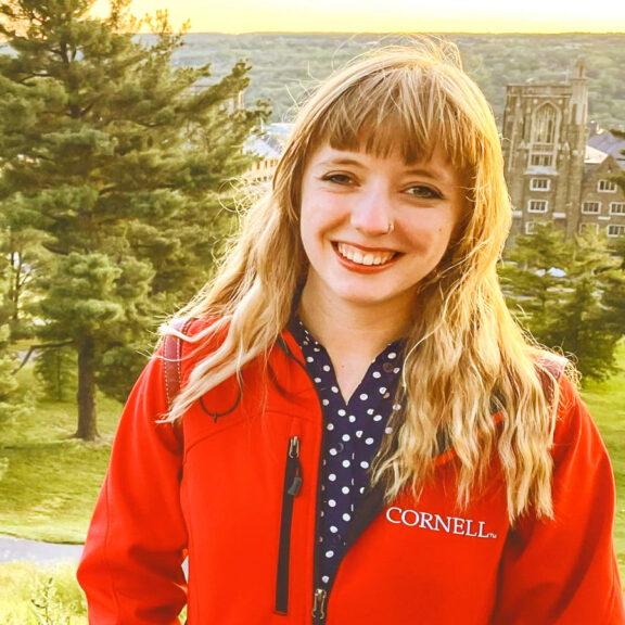 		Lorlei Boyd, long blond hair and in a Cornell jacket, smiling with Libe Slope trees behind her
	