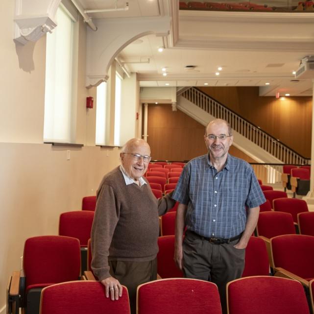 		Roald Hoffmann standing in a big lecture hall with one hand on Jeff Fearn's back, with the periodic table on the wall to their left, both smiling and rdressed casually.
	
