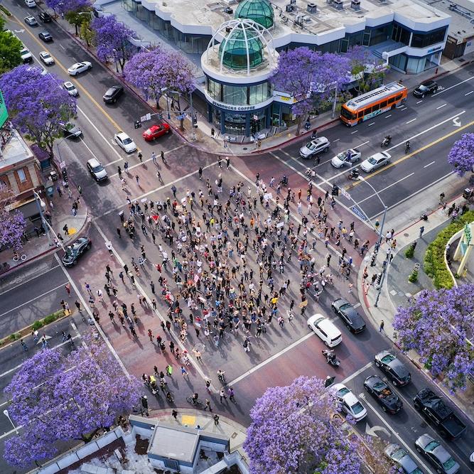 		A crowd gathering on a city intersection, seen from above
	
