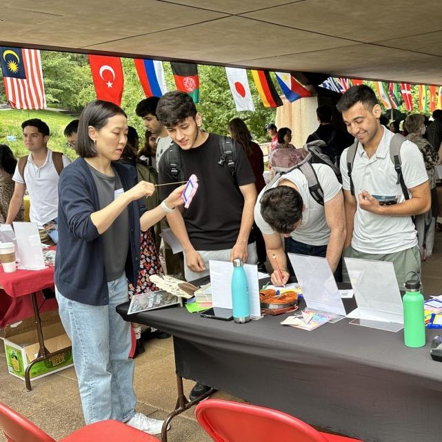 		Several people cluster around a table with international flags in the background
	