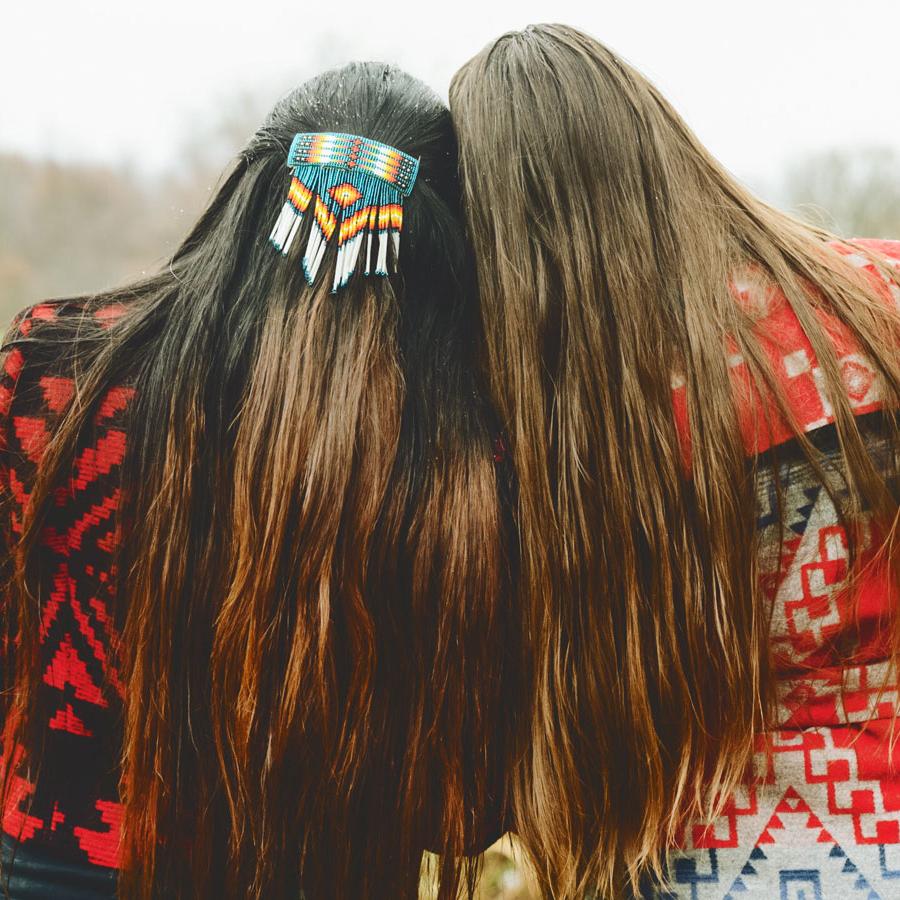 Two women with long hair and wearing Native American-patterned clothing and hairpiece.