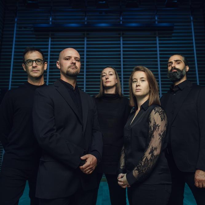 		Five people wearing black pose against a blue and black background. They look forboding.
	