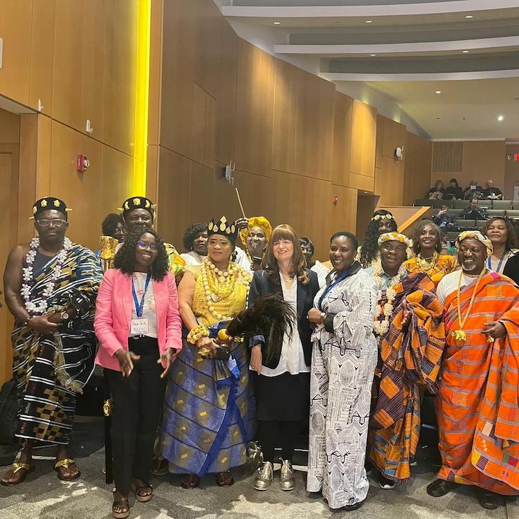 		Sevral people, some in colorful traditional dress, stand together in an auditorium
	