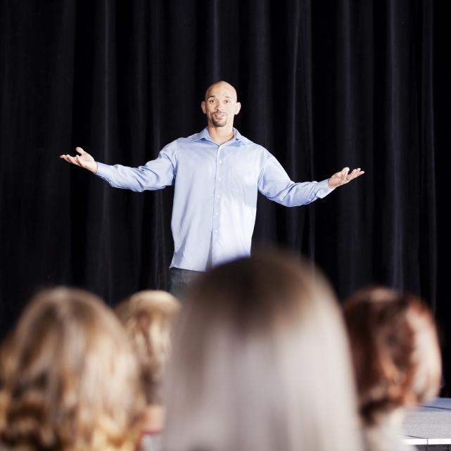 Person standing on a stage with arms spread