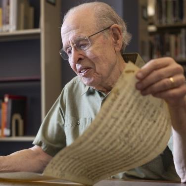 		Neal Zaslaw, in glasses and short-sleeved button-down shirt, looking at a musical score long enough that he is holding it in both hands.
	