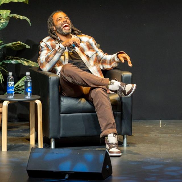 		Two people on a stage, sitting in arm chairs, holding microphones
	