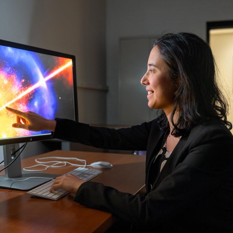 Anna Ho sitting at desk, pointing at computer screen with image of star exploding