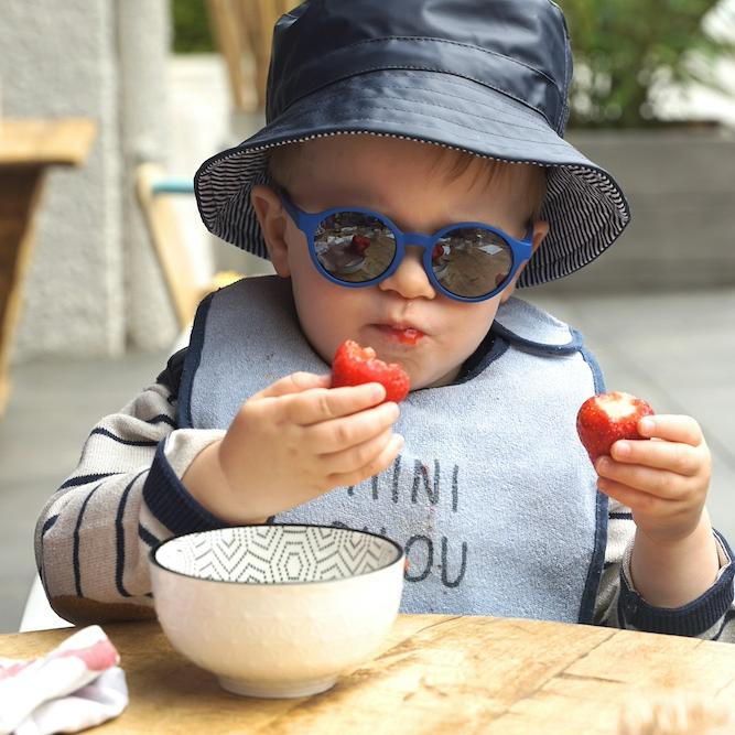 		child wearing sunglasses, holding two strawberriers
	