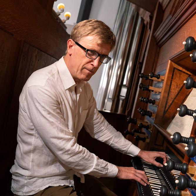 Person sitting at the consol of a wooden organ, hands on keyboard