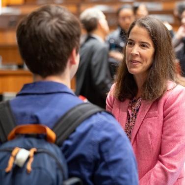 Ann Marimow in pink jacket and long brown hair speaks to a student wearing a backpack with his back to her.