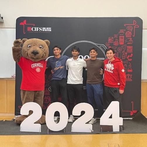 		Four people stand with a mascot bear 
	