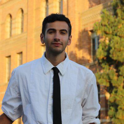 		Jeremy Peschard Pórtela with white shirt and black tie, a faint beard and mustache, in front of a sunlight building.
	