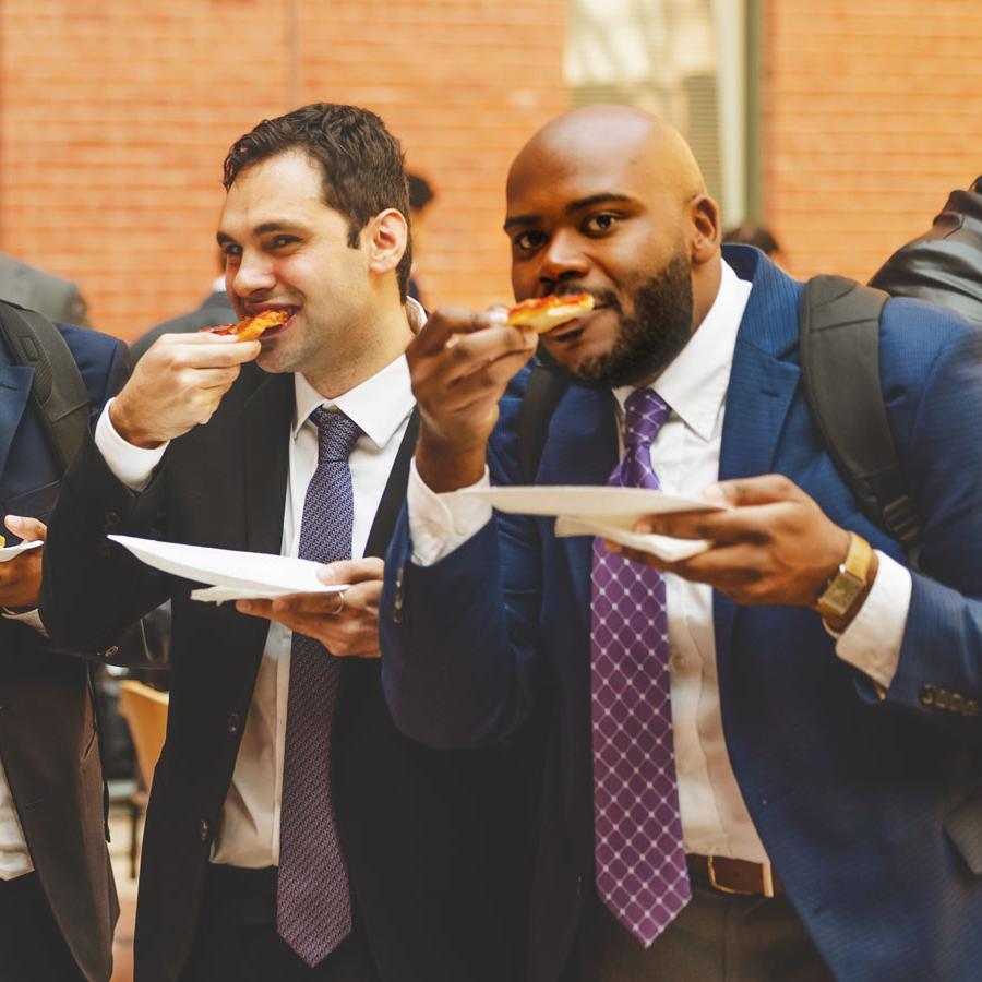 		Four people wearing suits, all chomping on slices of pizza and holding plates
	