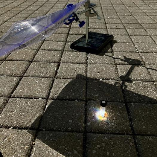 A glass vial sits in a patch of sunlight on a square tiled floor, with shadow around it.