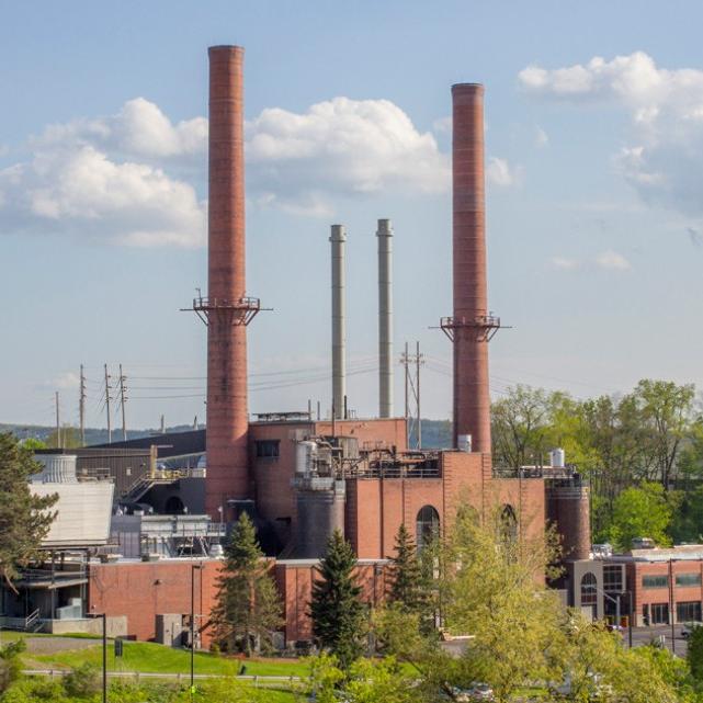 		large brick building with smoke stacks reaching into a blue sky studded with clouds
	