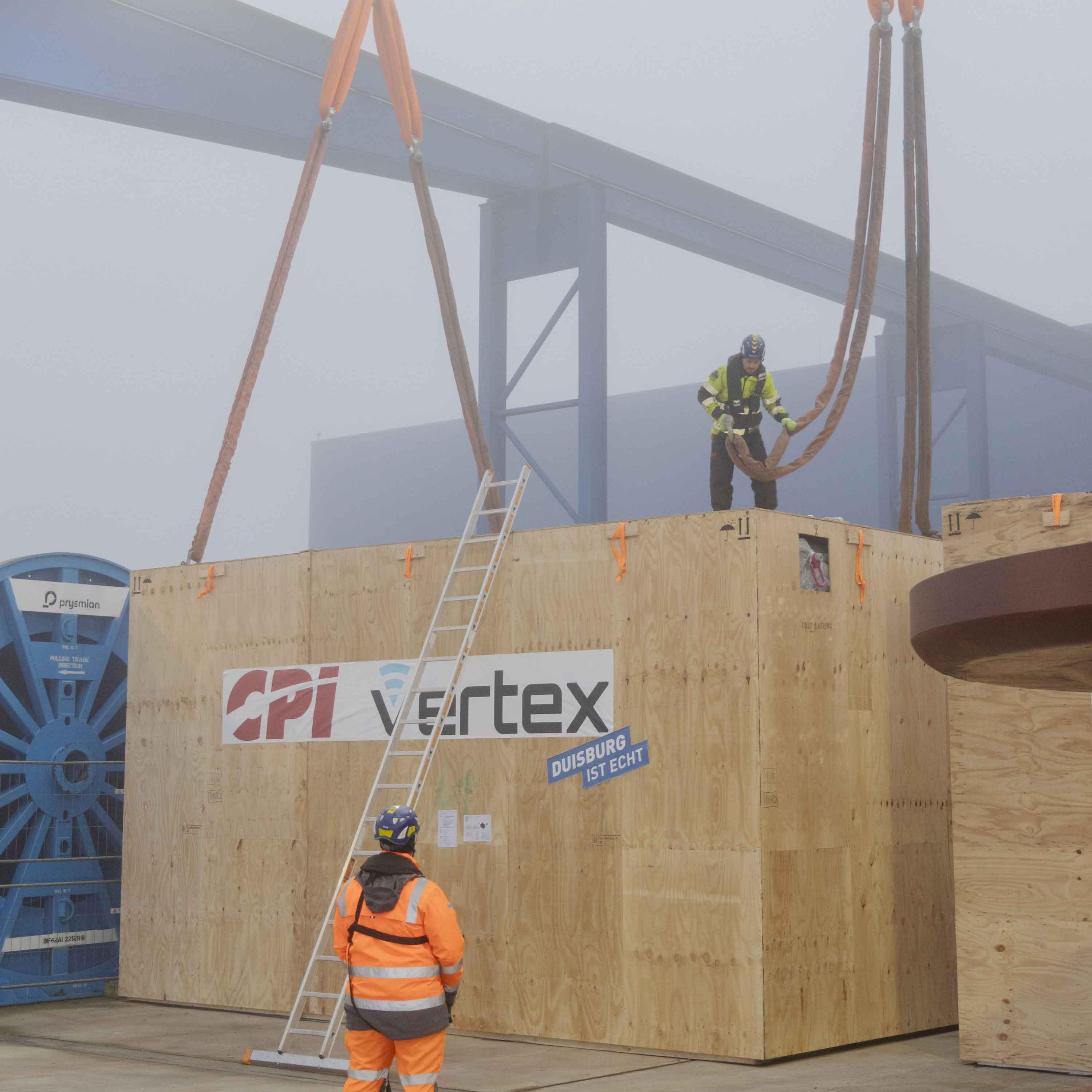 		Man standing on top of huge crate attaching a cable to it.
	