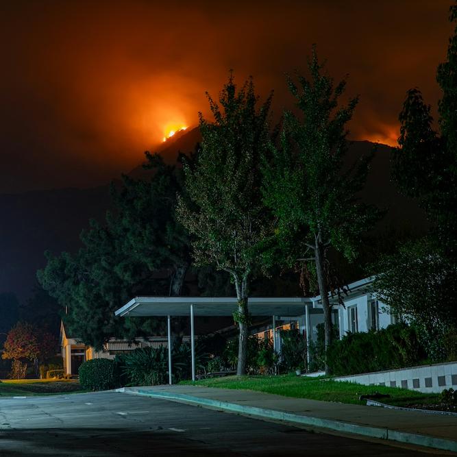 		A house and garden in the foreground at night, with a wildfire glowing over a nearby hill
	