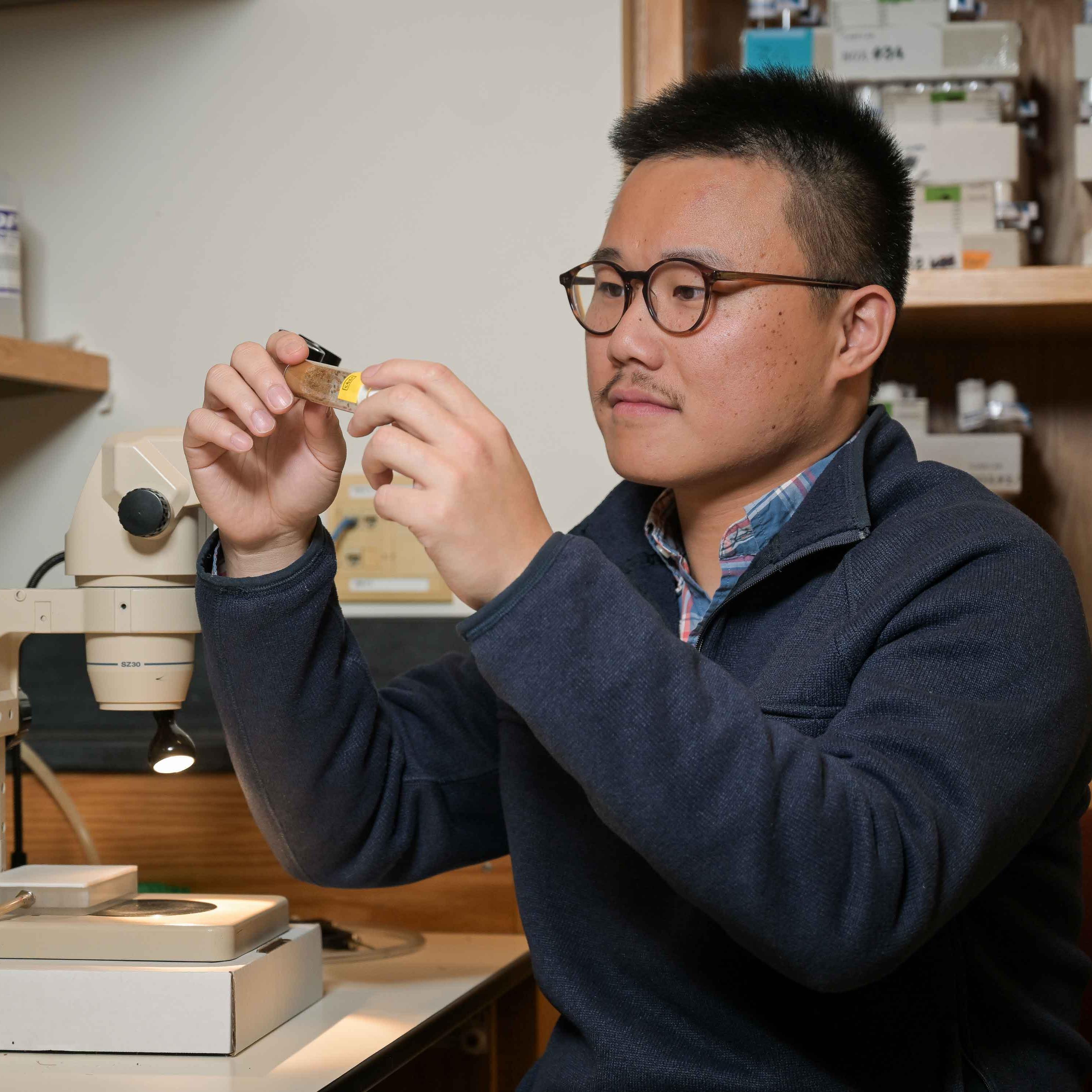 		Peiwei Chen with glasses in lab, holding up vial to look at
	