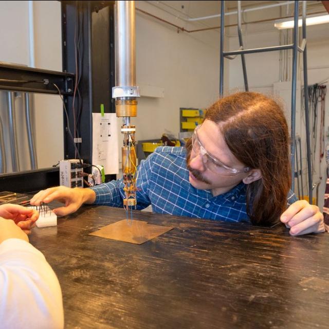 Three people wearing lab safety glasses look at a small scientific device