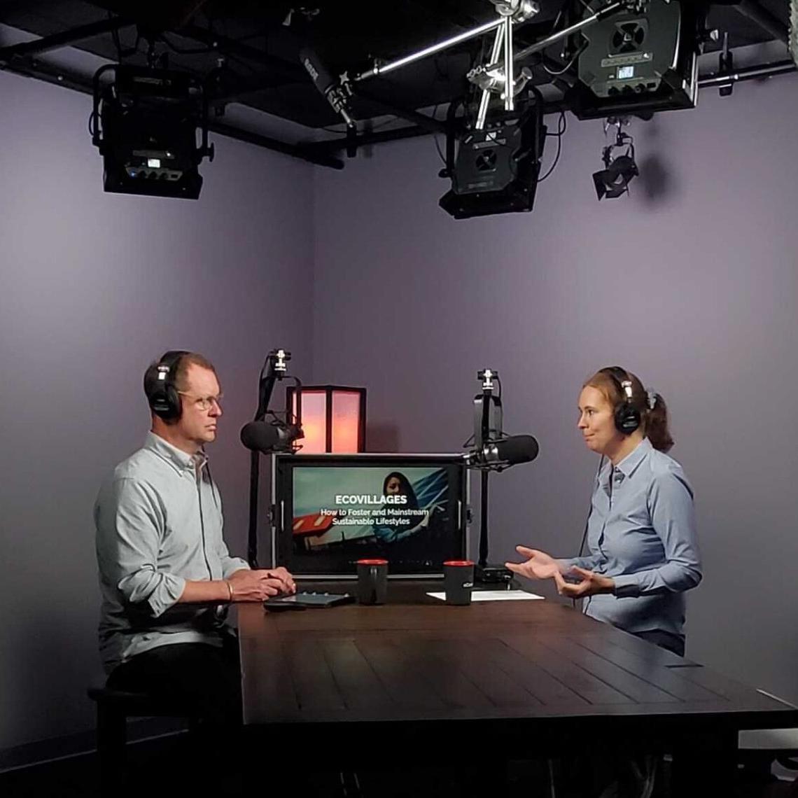 		Two people sit at a table in a recording studio
	