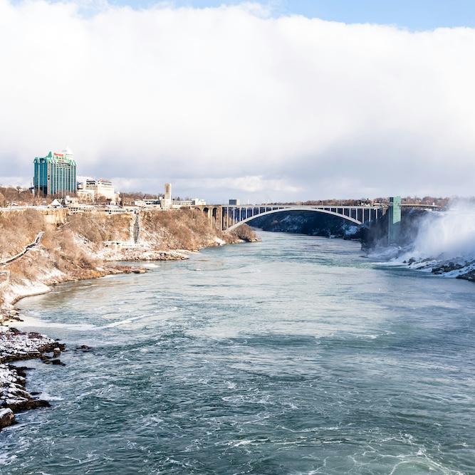 		A wide river dividing two banks with a bridge in the distance
	