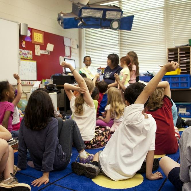 		Several children sit on a rug in a classroom
	