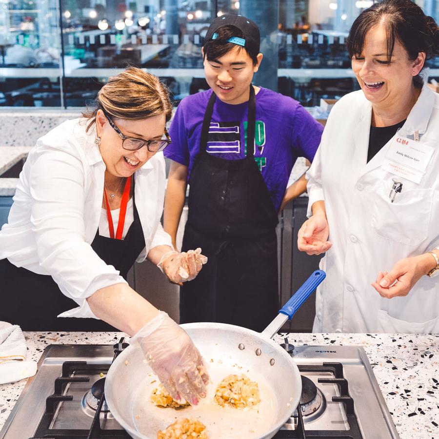 		three people cooking over a stove
	