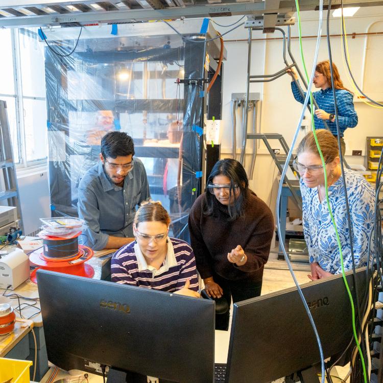 		Three people cluster around a computer in a science lab
	