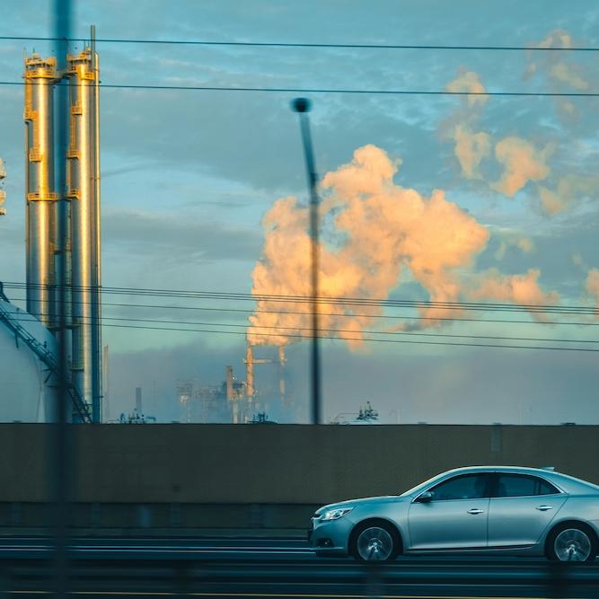 		Car driving past a factory belching smoke
	