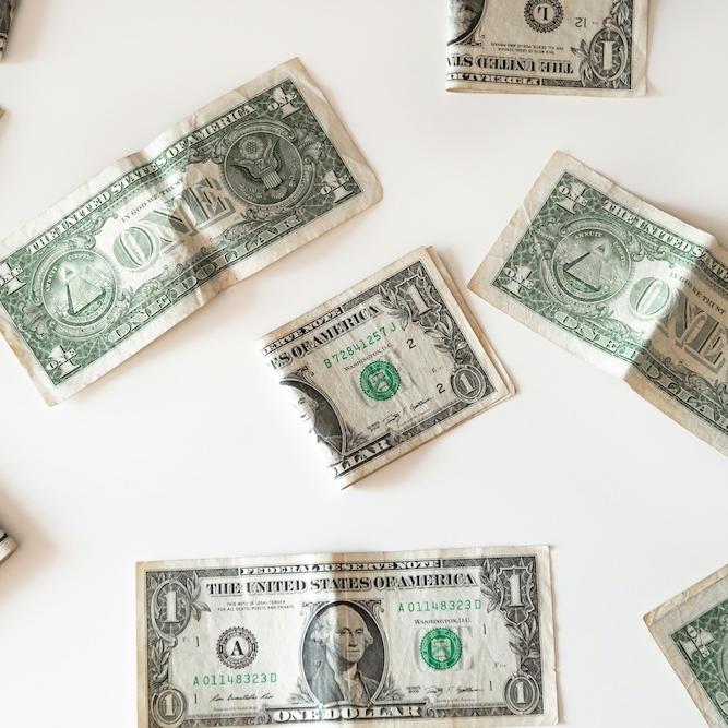 		Dollar bills, some of them folded and crumpled, resting on a white surface
	